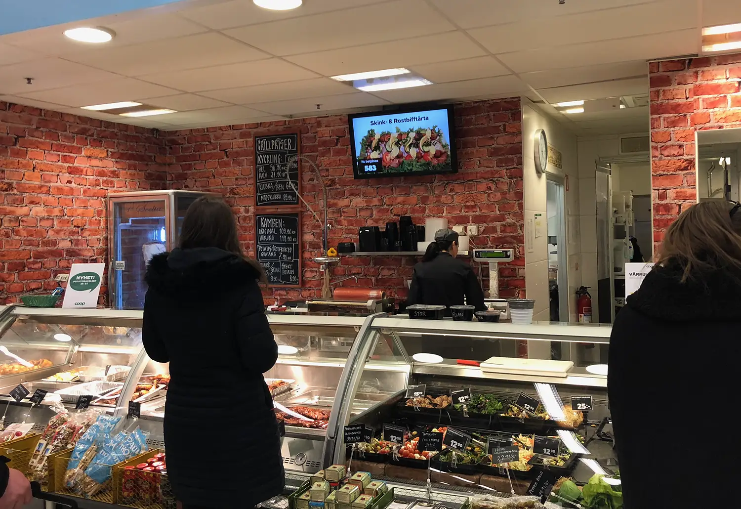 Digital skärm på vägg med kösystem i delikatessen